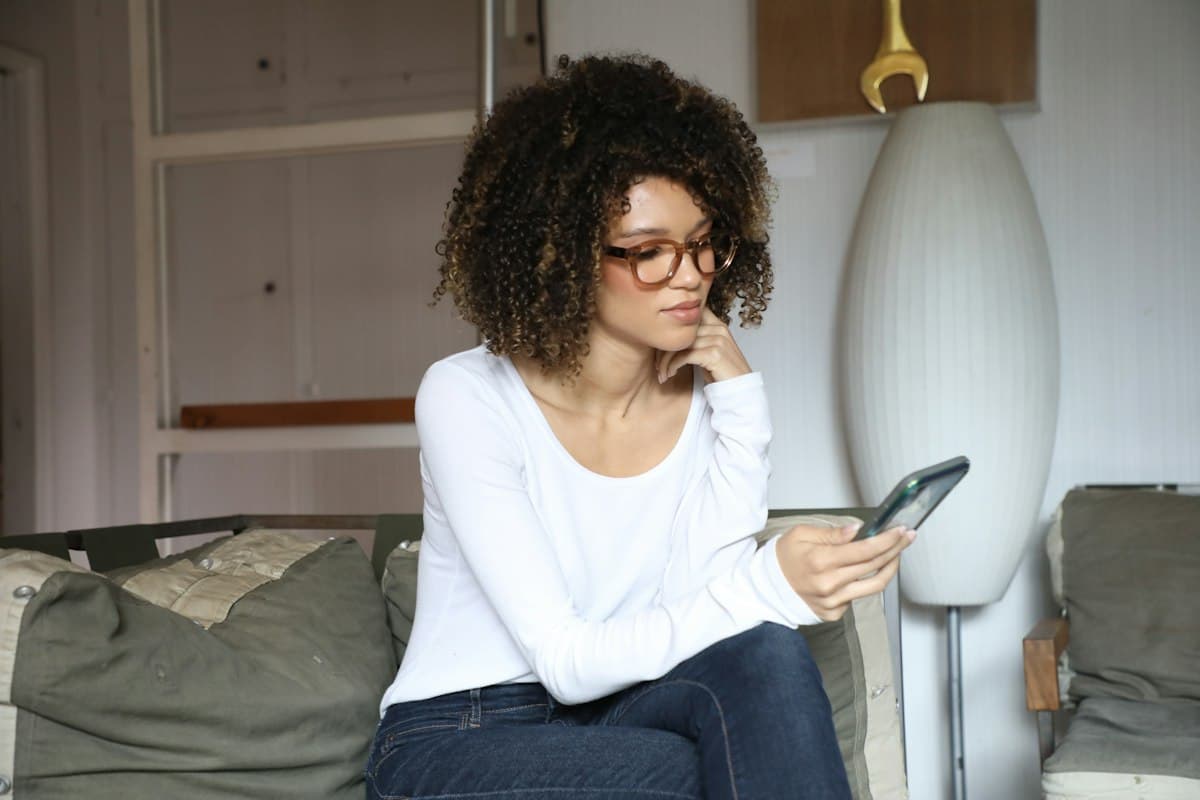 Femme pensive sur son canapé regardant son téléphone, anxiété relationnelle