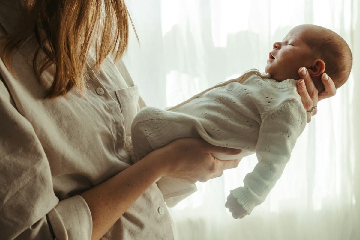 Mère tenant son nouveau-né près d'une fenêtre, douleur au coccyx après l'accouchement