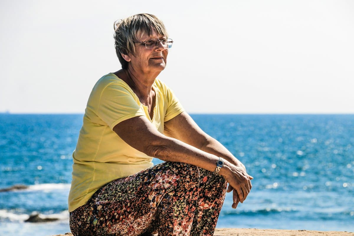 Femme de plus de 50 ans assise au bord de la mer, douleurs articulaires à la ménopause