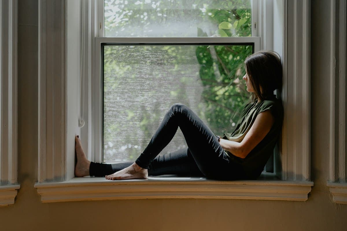 Femme pensive assise près d'une fenêtre, hypocondrie et peur d'être malade