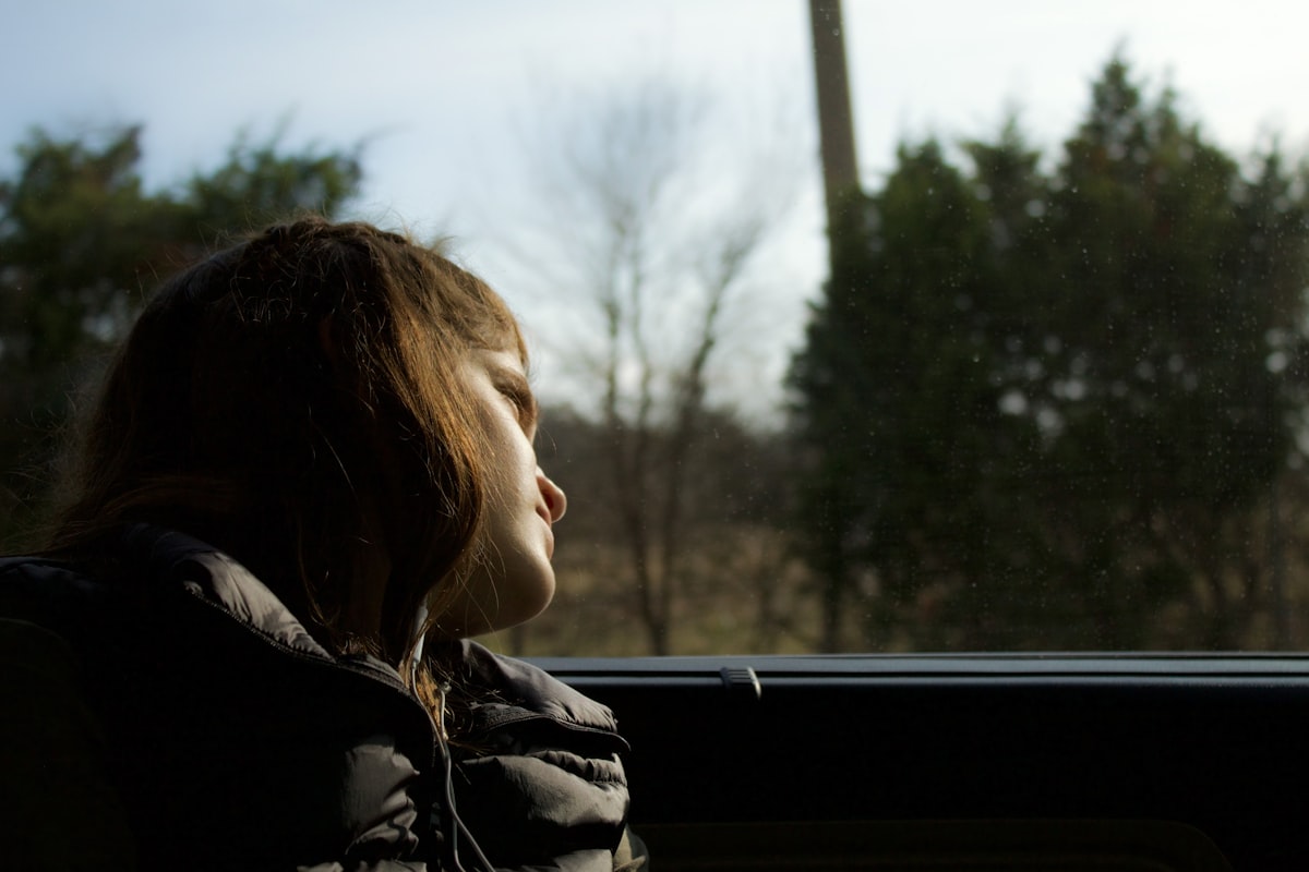 Jeune maman pensive près d'une fenêtre, signes de dépression post-partum