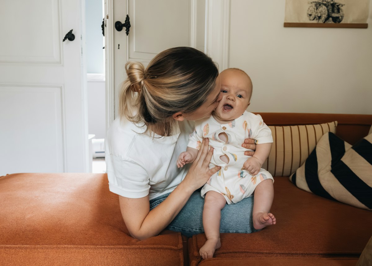 Jeune maman assise sur un canapé avec son bébé, douleur au coccyx après l'accouchement