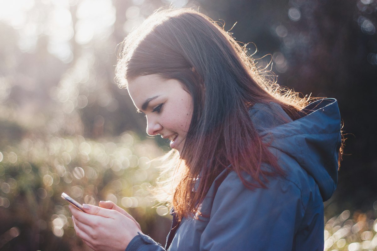 Femme souriante consultant son téléphone en extérieur, sereine après son échographie de contrôle du stérilet