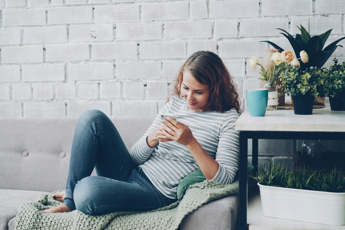 Femme détendue sur son canapé, téléphone en main, sans chercher ses symptômes en ligne