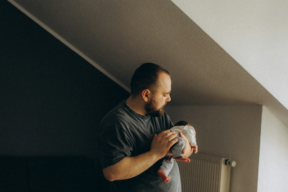 Jeune père tenant tendrement son bébé près d'une fenêtre, pensées intrusives post-partum