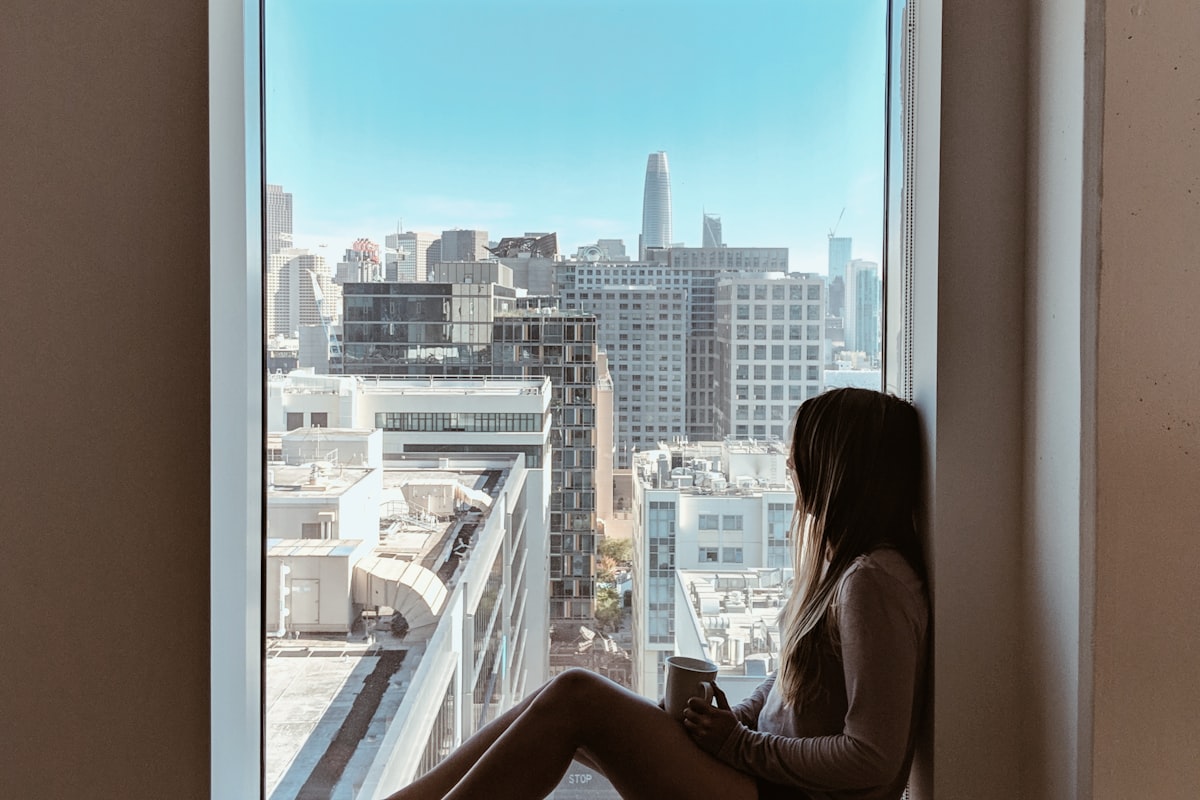 Femme pensive traversant l'impact psychologique d'une blessure, près d'une fenêtre