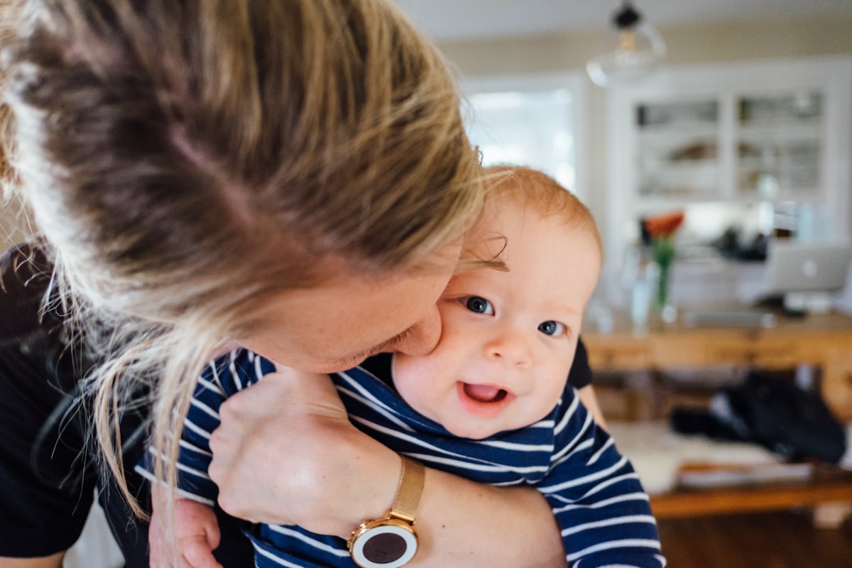 Mère câlinant son bébé souriant à la maison, suivi du nourrisson